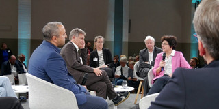 Wir haben die besten Spieler Eine Podiumsdiskussion mit fünf Teilnehmenden, die im Kreis sitzen. Eine Frau spricht in ein Mikrofon, während die anderen zuhören. Im Hintergrund ist ein Publikum zu sehen.