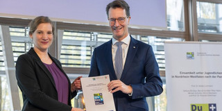 Foto: Ministerpräsident Hendrik Wüst und Prof. Maike Luhmann halten eine Urkunde in die Kamera.