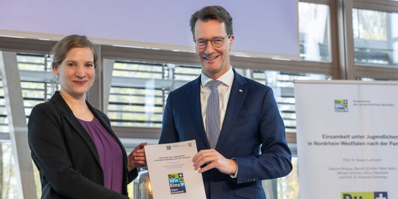 Foto: Ministerpräsident Hendrik Wüst und Prof. Maike Luhmann halten eine Urkunde in die Kamera.