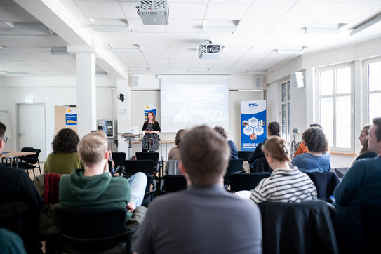 Seminarraum, in dem Vorne eine Referentin steht, das Auditorium ist von hinten zu sehen