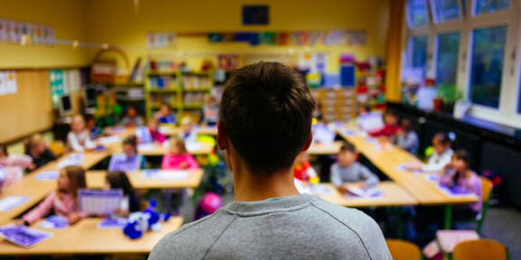 Lehrperson steht vor einer Schulklasse.