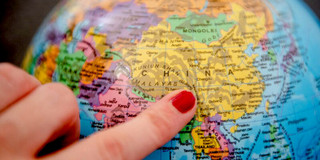 Ein Finger, der auf einem Globus auf das Land China zeigt.