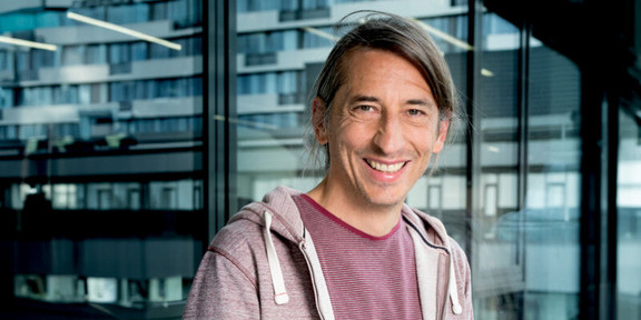 Foto: Ein Porträt von Prof. Eike Kitz, einem Wissenschaftler mit langen Haaren und einem lila Pullover.