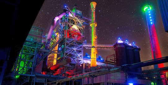 Nächtliche Aufnahme bunt illuminierter Industrieanlagen im Landschaftspark Duisburg-Nord