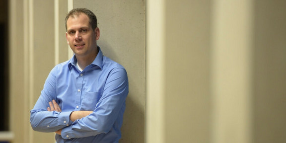 Prof. Neider, der vor einer weißen Wand lehnt.