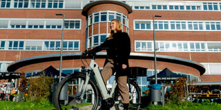 Eine Frau, die mit einem E-Bike vor einem großen Gebäude steht.
