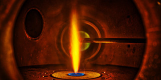 Die Mitte eines Synthesereaktors: Zu sehen ist eine Sprayflamme innerhalb eines Gehäuses aus Metall.