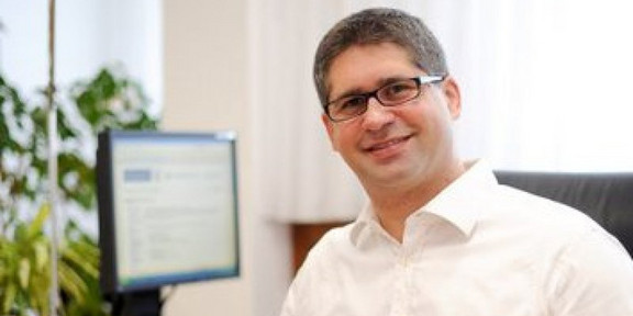 Das Bild zeigt Prof. Sven Rahmann am Schreibtisch sitzend. Er trägt eine Brille mit schwarzem Rahmen und ein langärmeliges weißes Hemd.