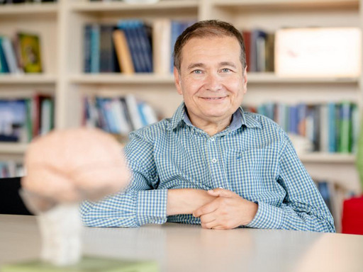Portraitfoto von Professor Güntürkün sitzend, auf dem Tisch vor ihm ein Gehirnmodell