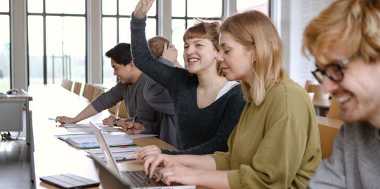 Hörsaal mit Studierenden, von denen sich eine Studentin meldet.