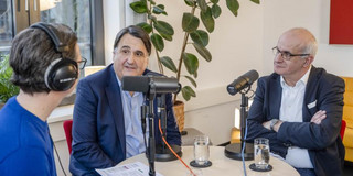 Drei Personen sitzen an einem runden Tisch.