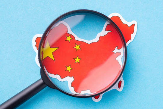 A magnifying glass lies on a map of China, which is designed like the Chinese flag, red with yellow stars