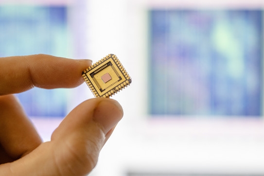 cropped section of index finger and thumb holding a gold-colored microchip