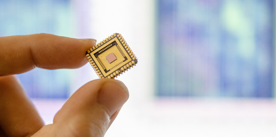 cropped section of index finger and thumb holding a gold-colored microchip