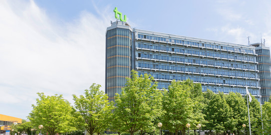 Campus Nord der TU Dortmund mit Blick auf den Mathetower an einem sonnigen Tag, im Vordergrund belaubte Bäume, 