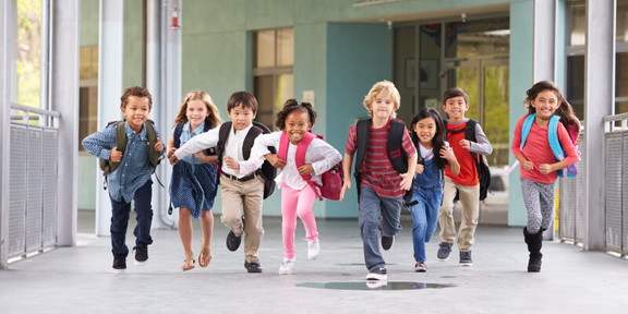 Eine Gruppe von Kindern, die mit Rucksäcken in eine Richtung läuft.