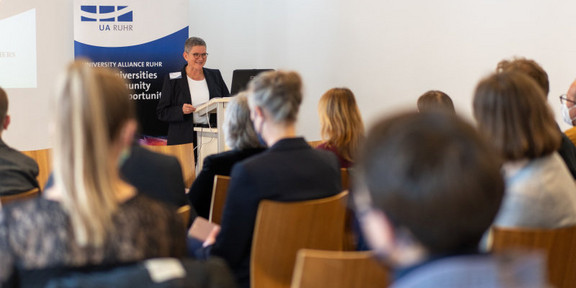 Isolde Karle steht vor sitzendem Publikum und hält eine Rede.