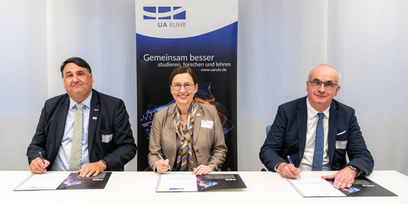 Photo: Two men and a woman in formal dress sit at a table and sign a declaration. Behind them hangs a banner of the UA Ruhr. The people are (from left to right): Joint signing of the Magna Charta Universitatum 2020 by the University Alliance Ruhr: the Rector of Ruhr-Universität Bochum, Prof. Martin Paul, the Rector of the University of Duisburg-Essen, Prof. Barbara Albert, and the Rector of TU Dortmund University, Prof. Manfred Bayer.