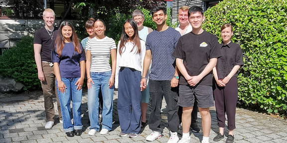 Eight students in front of a bush.