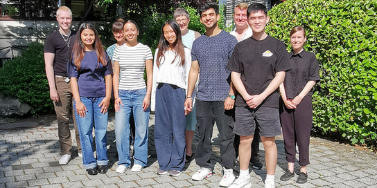 Eight students in front of a bush.