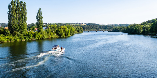 Sommerliches Foto der Ruhr mit grünen Ufern, auf dem Fluss fährt ein kleines Motorboot
