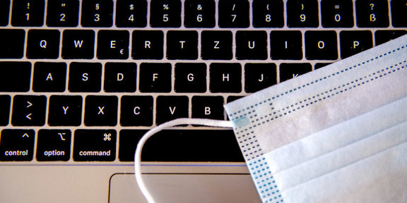 Laptop-Tastatur, auf der ein Mundschutz liegt