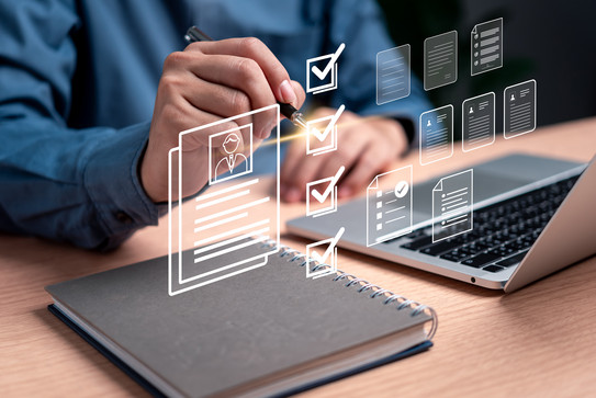 Person sitting at a desk with an open laptop and notebook, who is checking off an item that is superimposed over the image along with other graphic symbols