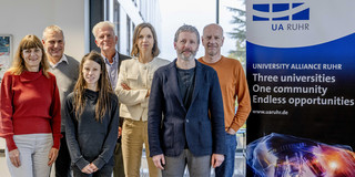 Foto: Ein Gruppenfoto vom UA Ruhr Rat für Ethik und Verantwortung neben einem Aufsteller der UA Ruhr. Auf dem Aufsteller steht: "University Alliance Ruhr. Three universities, one community, endless opportunities"