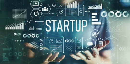 Graphic photo montage showing a person with their hands stretched out in front of them in the foreground. Above their hands are the words “Startup” and numerous symbols from science and technology.