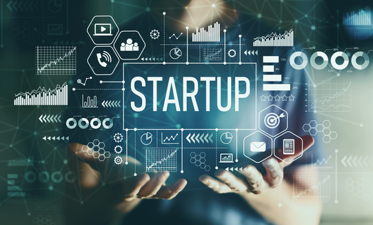 Graphic photo montage showing a person with their hands stretched out in front of them in the foreground. Above their hands are the words “Startup” and numerous symbols from science and technology.