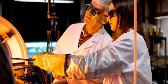Foto: Zwei Personen in Kitteln und Schutzbrillen arbeiten in einem Labor.