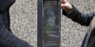 Das Bild zeigt den Science Award, der von zwei Personen gehalten wird.