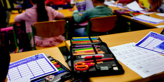 Nahaufnahme eines Tisches in einer Schulklasse. Auf dem Tisch liegen zwei Etuis, die mit Stiften gefüllt sind, und ein Stundenplan