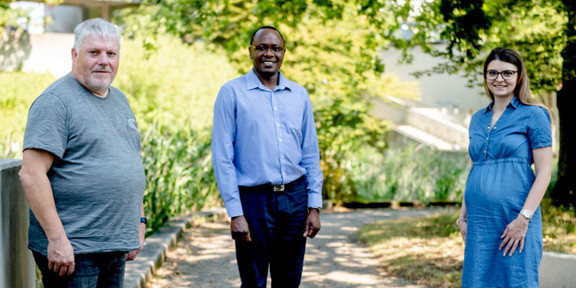 Foto: Drei Personen stehen mit Abstand zu einander auf dem sonnigen und grünen Campus der Ruhr-Universität Bochum.
